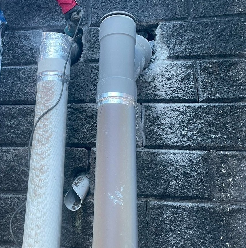 周囲のコンクリート部分を丁寧にはつりながら既設配管を撤去している写真